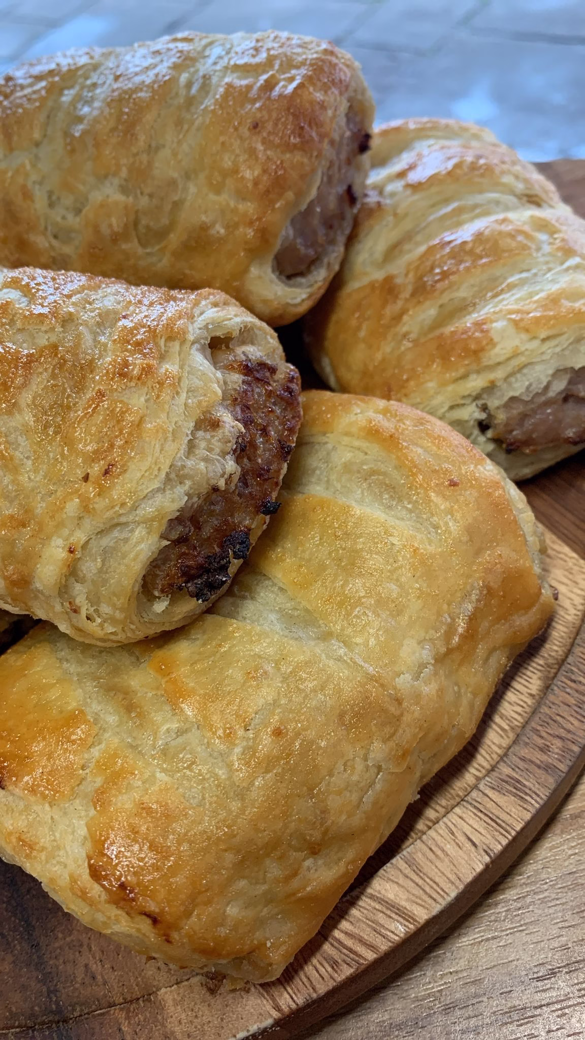 A close-up of freshly baked homemade sausage rolls with golden, flaky pastry, resting on a wooden board.