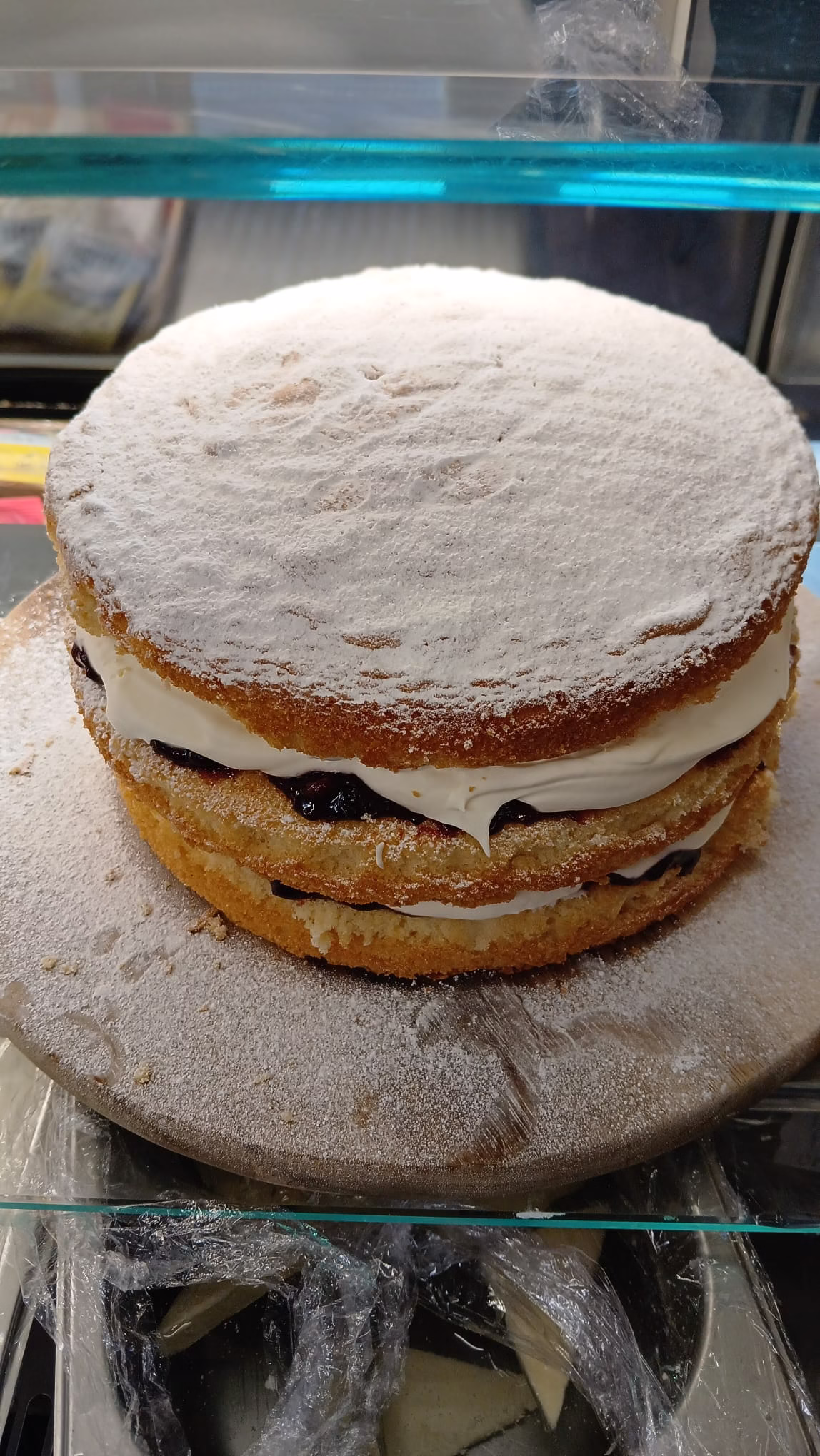 A classic Victoria sponge cake with layers of jam and cream, dusted generously with icing sugar, displayed on a glass cake stand.