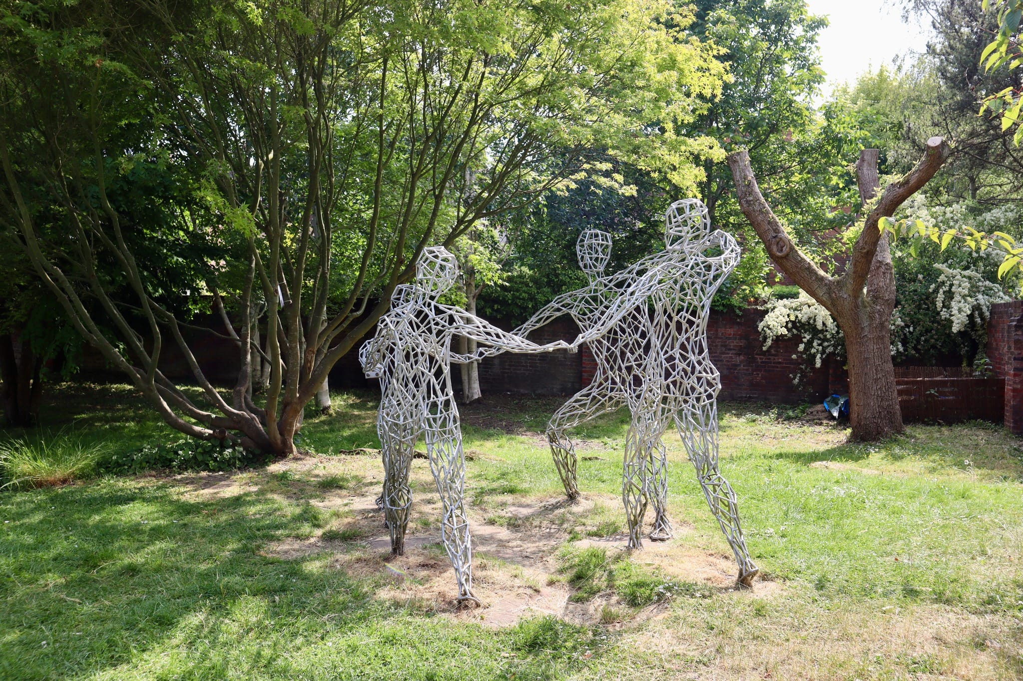 Jubilation Sculpture by Lucy Unwin in Jubilee Gardens, Bewdley Jubilation, a striking wireframe sculpture by Gloucestershire artist Lucy Unwin, located in Jubilee Gardens, Bewdley. The piece depicts three abstract human figures holding hands, set against a lush green backdrop.