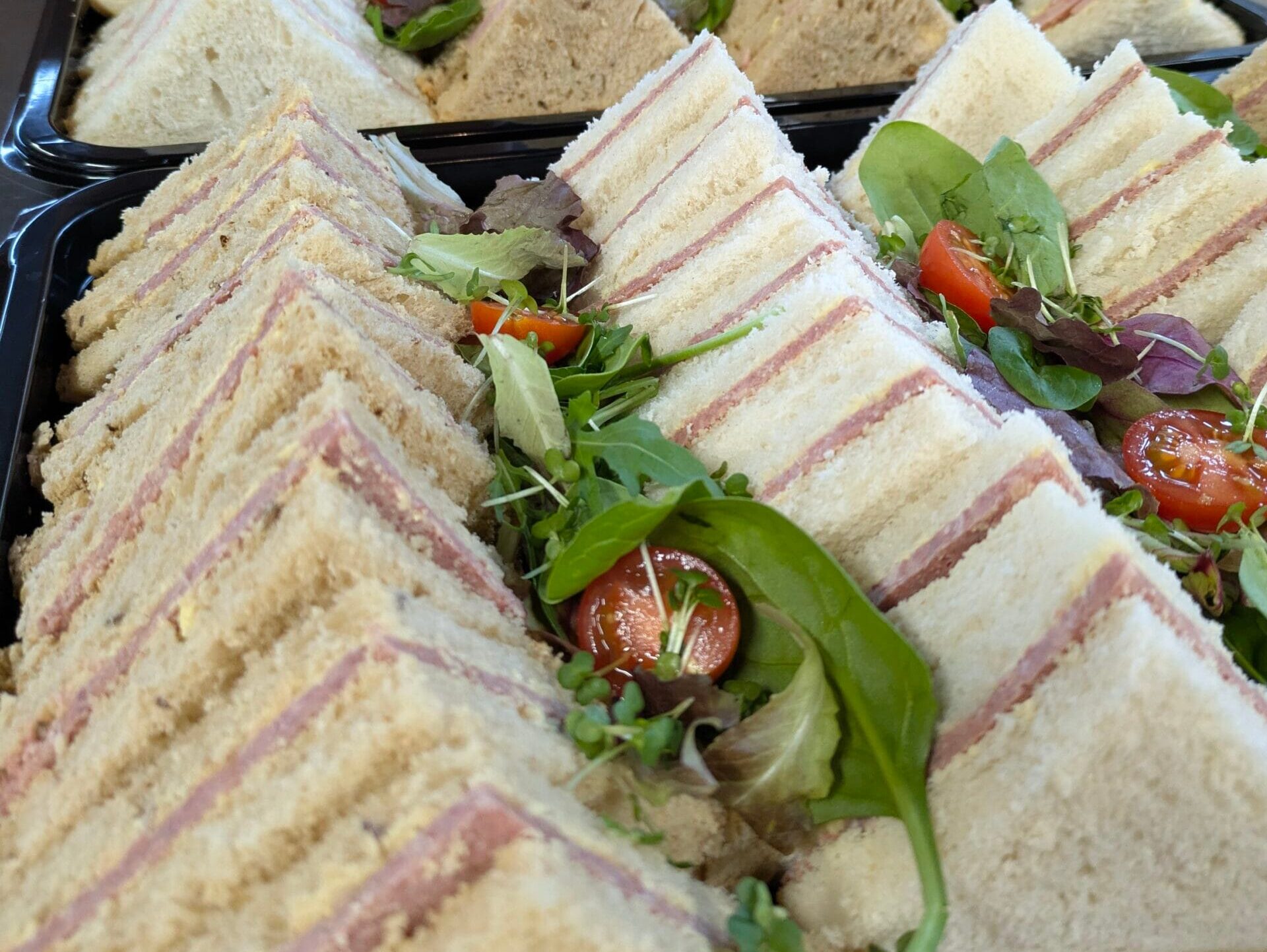 Catering sandwich platters with mixed bread finger sandwiches, salad leaves and cherry tomatoes.