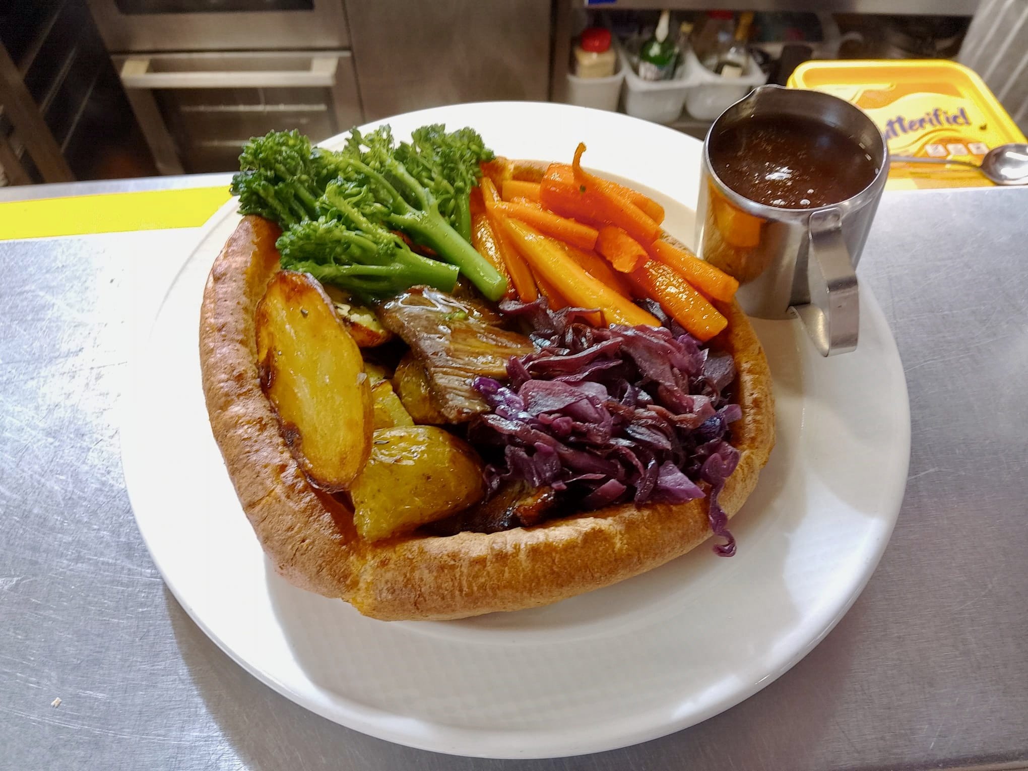 Roast beef, mixed local vegetables, and roast potatoes served inside a large Yorkshire pudding with a side jug of gravy.
